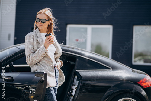 Young happy woman drinking coffee by the car