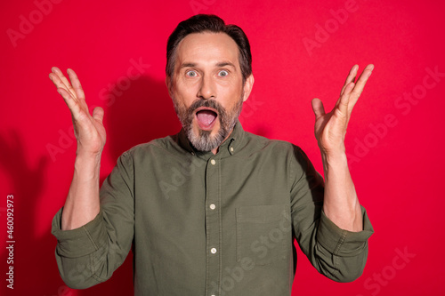 Photo of impressed age brunet man hands up wear green shirt isolated on red color background