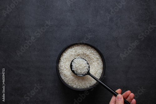 Rice in bowl and spoon on dark grey background.