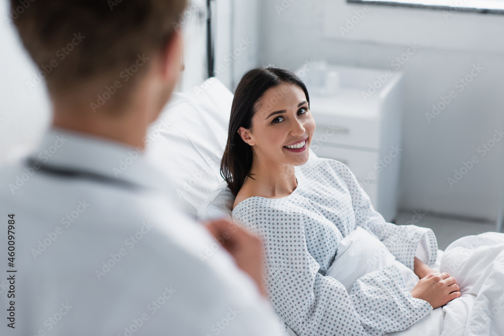 positive woman in patient gown looking at blurred doctor in white coat positive woman in patient gown looking at blurred doctor in white coat