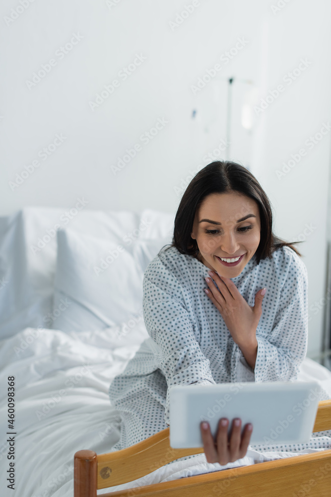 flattered woman in patient gown smiling during video call in hospital