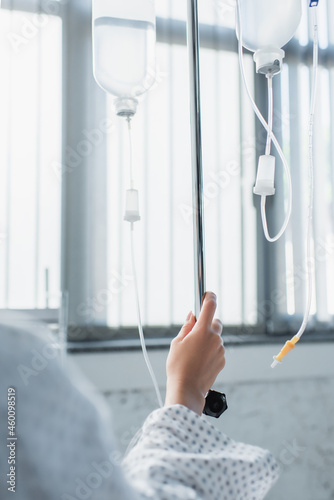 cropped view of sick woman holding hand on drop counter with intravenous therapy bottles