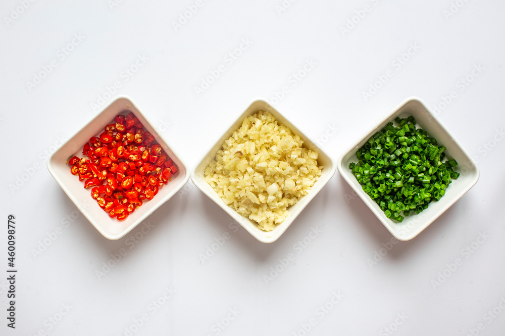 Chopped Green onion and Chili pepper and garlic in white plate on white background. top view. Chopped Green onion and Chili pepper and garlic in white plate on white background. top view.