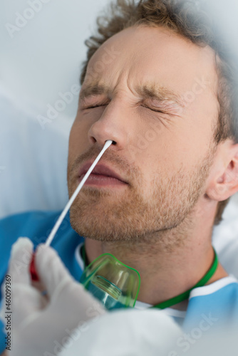 doctor holding swab near nose of patient with closed eyes while doing pcr test