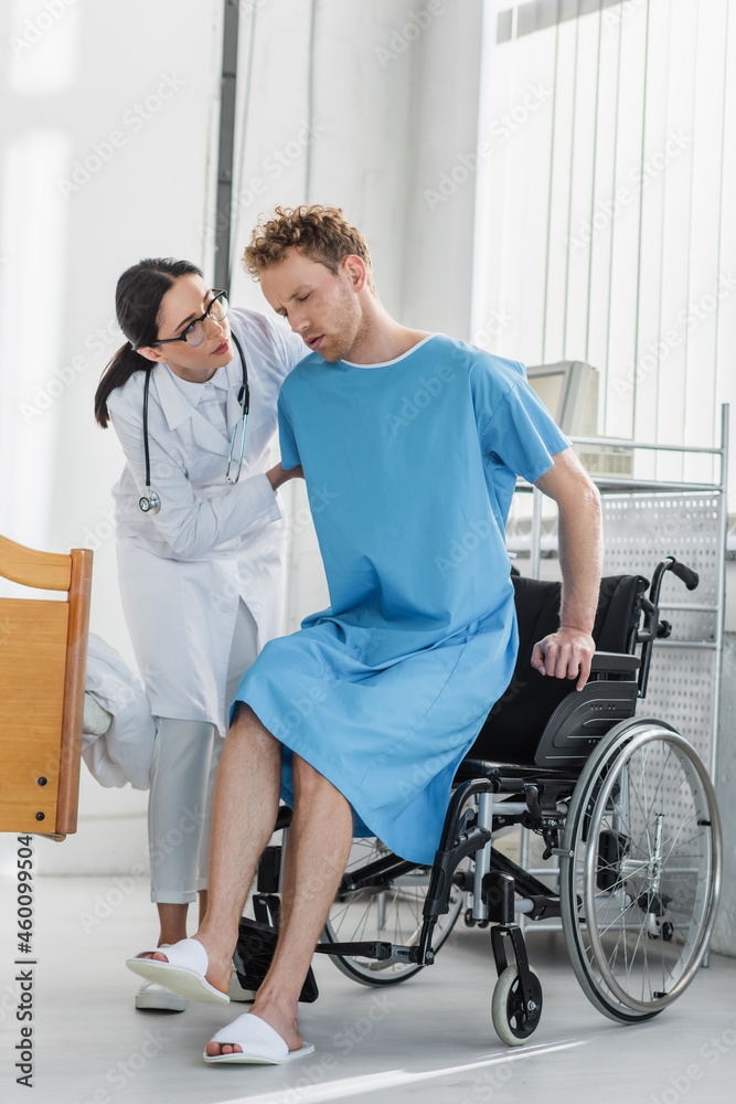 doctor in white coat helping disabled patient sit in wheelchair