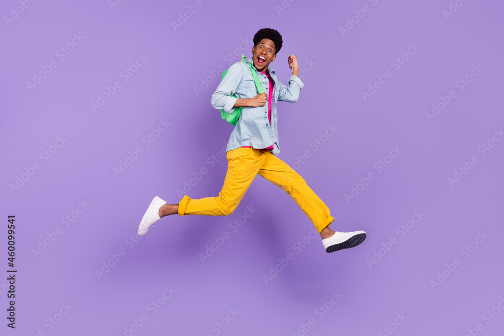 Photo of cheerful guy jump hurry run raise fist wear backpack blue shirt isolated purple color background