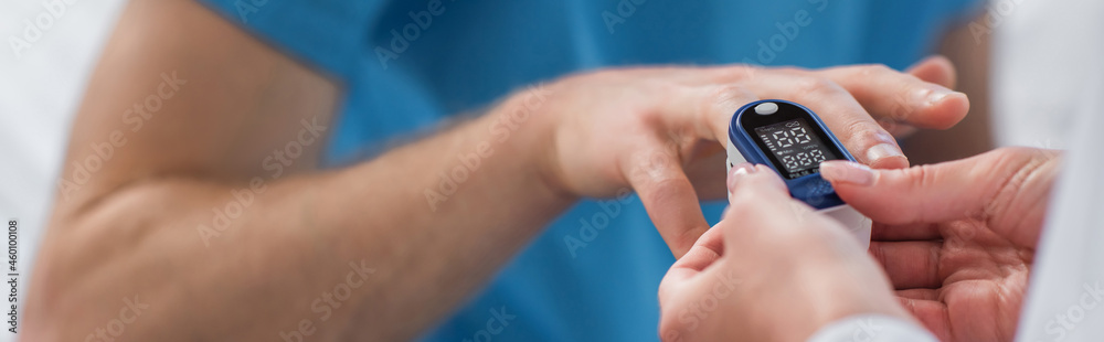 cropped view of doctor placing pulse oximeter on finger on patient in hospital, banner
