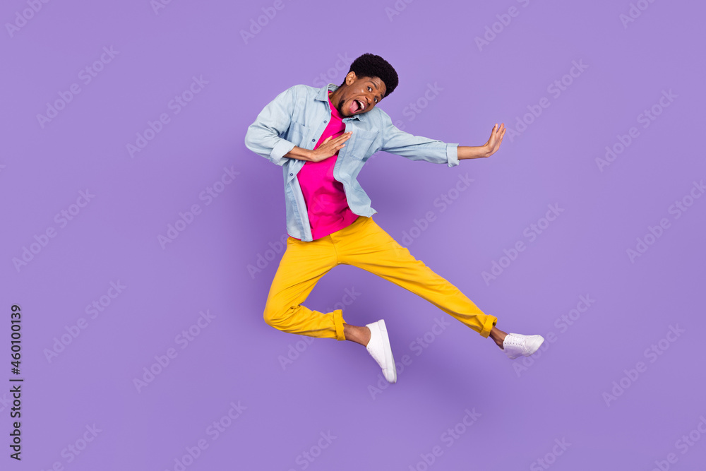 Photo of careless funky energetic guy jump kick leg wear blue shirt pants sneakers isolated purple color background