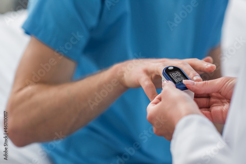 cropped view of doctor placing pulse oximeter on finger on patient in hospital