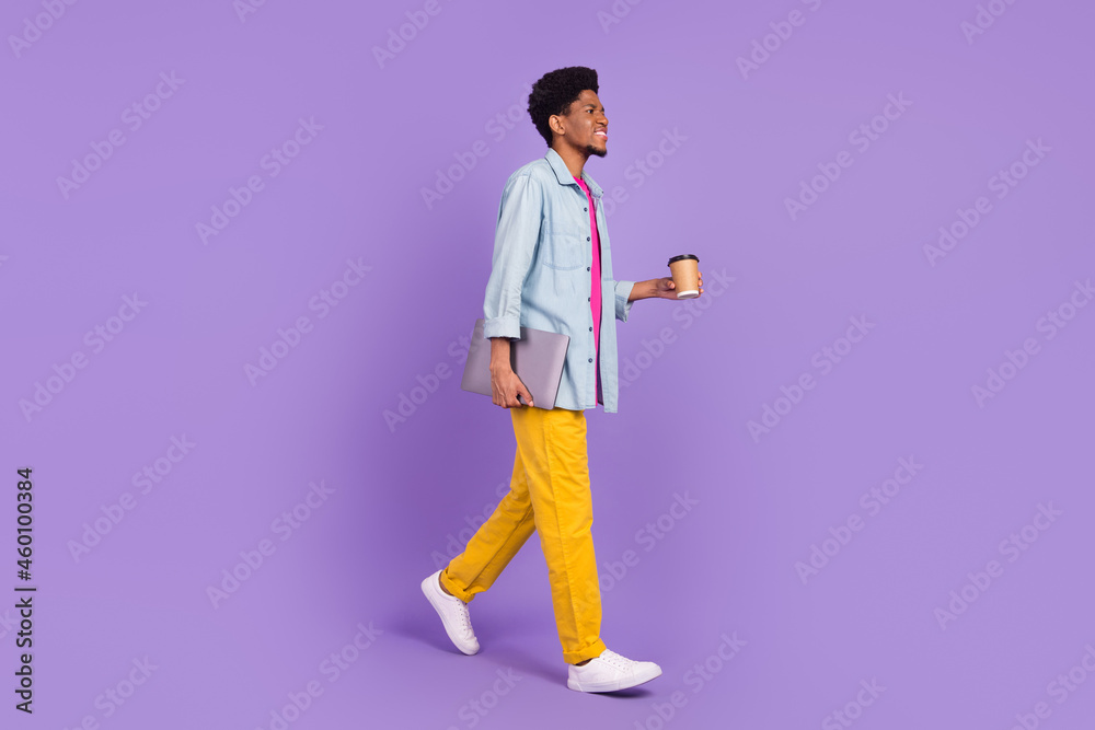 Photo of funky cute man wear denim walking drinking tea looking empty space holding gadget isolated purple color background Photo of funky cute man wear denim walking drinking tea looking empty space holding gadget isolated purple color background