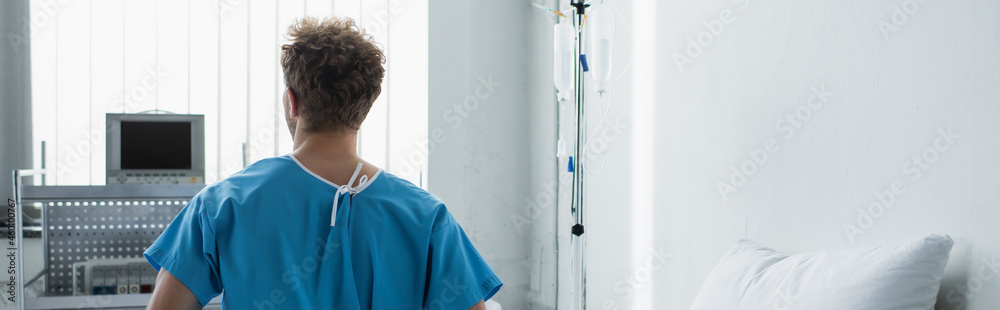 back view of curly man in patient gown sitting on hospital, banner back view of curly man in patient gown sitting on hospital, banner