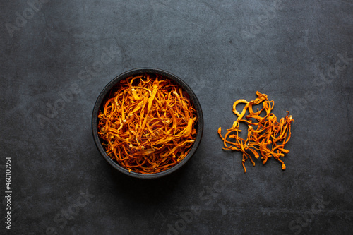 Dried cordyceps militaris mushroom in bowl on dark grey background. Cordyceps flower