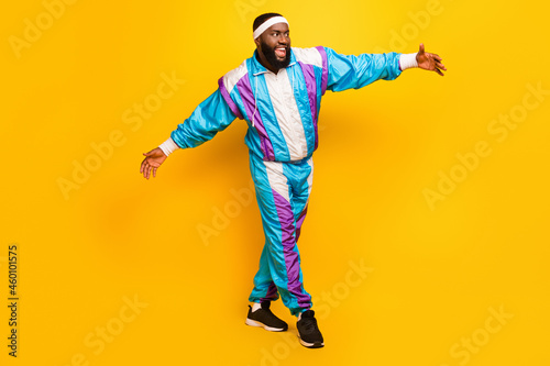 Photo of funny charming dark skin guy dressed sport suit headband smiling dancing walking isolated yellow color background © deagreez