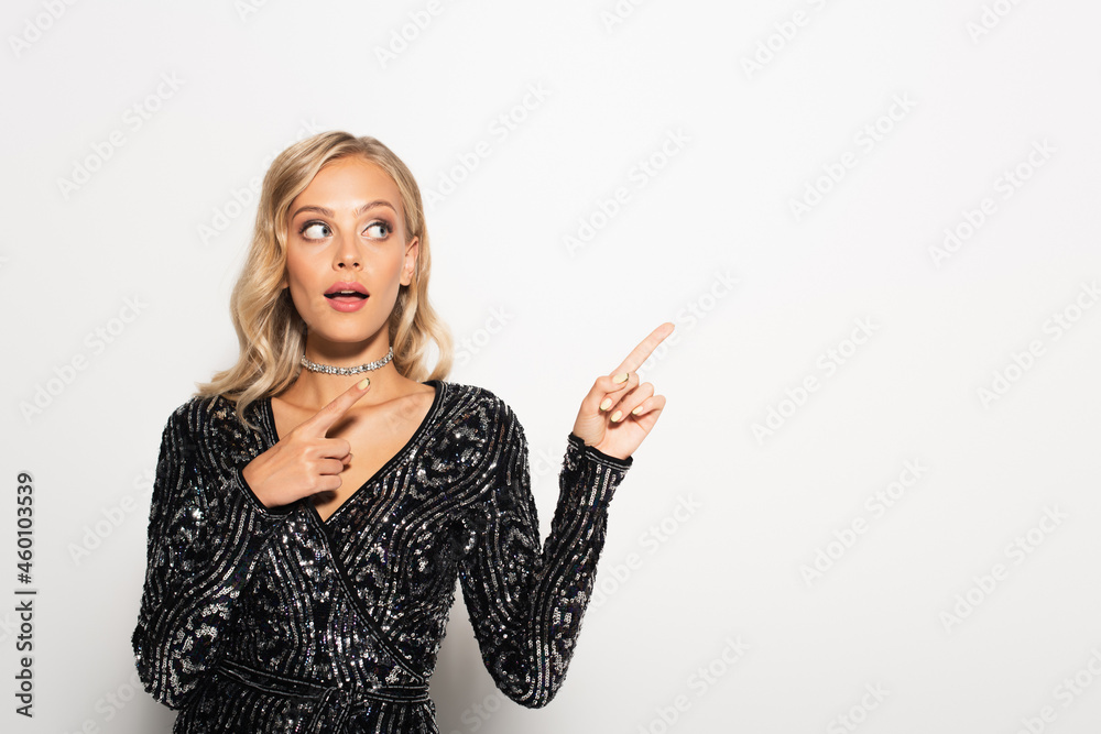 surprised blonde woman in black blouse with sequins looking aside and pointing with fingers on white surprised blonde woman in black blouse with sequins looking aside and pointing with fingers on white