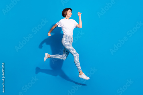 Photo of pretty hurrying young lady wear white outfit smiling walking running looking empty space isolated blue color background