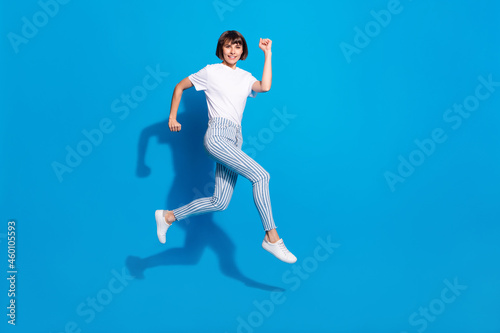 Photo of pretty charming young woman dressed casual clothes jumping running fast smiling isolated blue color background © deagreez