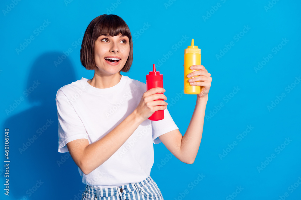 Photo portrait pretty girl smiling keeping ketchup mustard looking copyspace isolated vibrant blue color background Photo portrait pretty girl smiling keeping ketchup mustard looking copyspace isolated vibrant blue color background