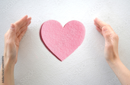 Hands surrounding a pink heart  symbol of love and care