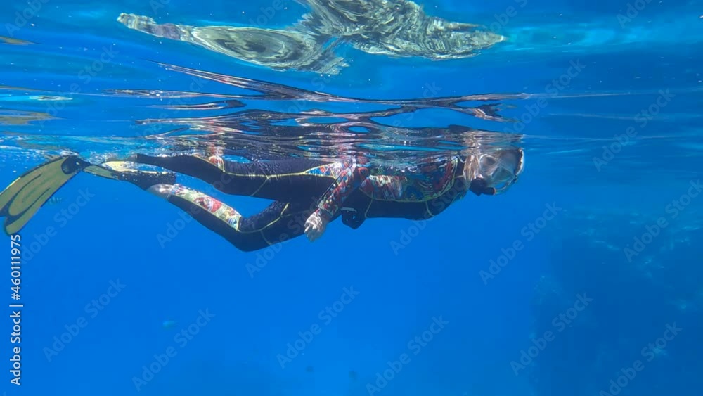 Slow motion. Woman in diving equipment swimming on the surface of blue water and looks at on marine life. Female snorkeler swims underwater and looking on underwater world. Slow motion. Woman in diving equipment swimming on the surface of blue water and looks at on marine life. Female snorkeler swims underwater and looking on underwater world.