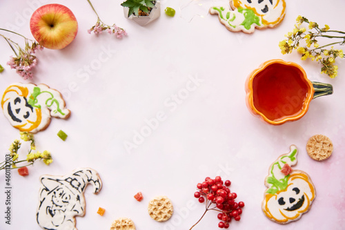 Halloween festive background: pumpkin cup and cookies in shape of cute pumpkins and ghost. Atmospheric aesthetic autumn mood or trick or treat concept. Apples, dry flowers and candied fruit