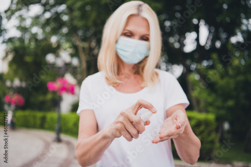 Photo of aged nice blond lady desinfect hands wear mask white t-shirt in park alone