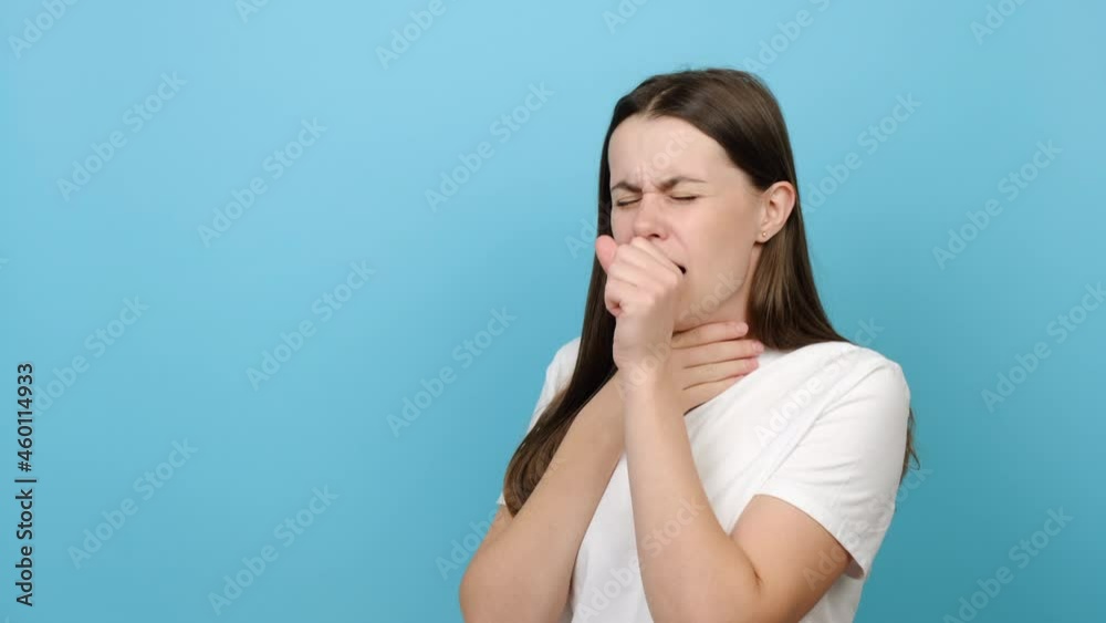 Unhealthy female standing isolated over blue background covers her mouth with hand while coughing, suffers from seasonal grippe or bronchitis chronic disease. Woman having pneumonia symptoms concept Unhealthy female standing isolated over blue background covers her mouth with hand while coughing, suffers from seasonal grippe or bronchitis chronic disease. Woman having pneumonia symptoms concept