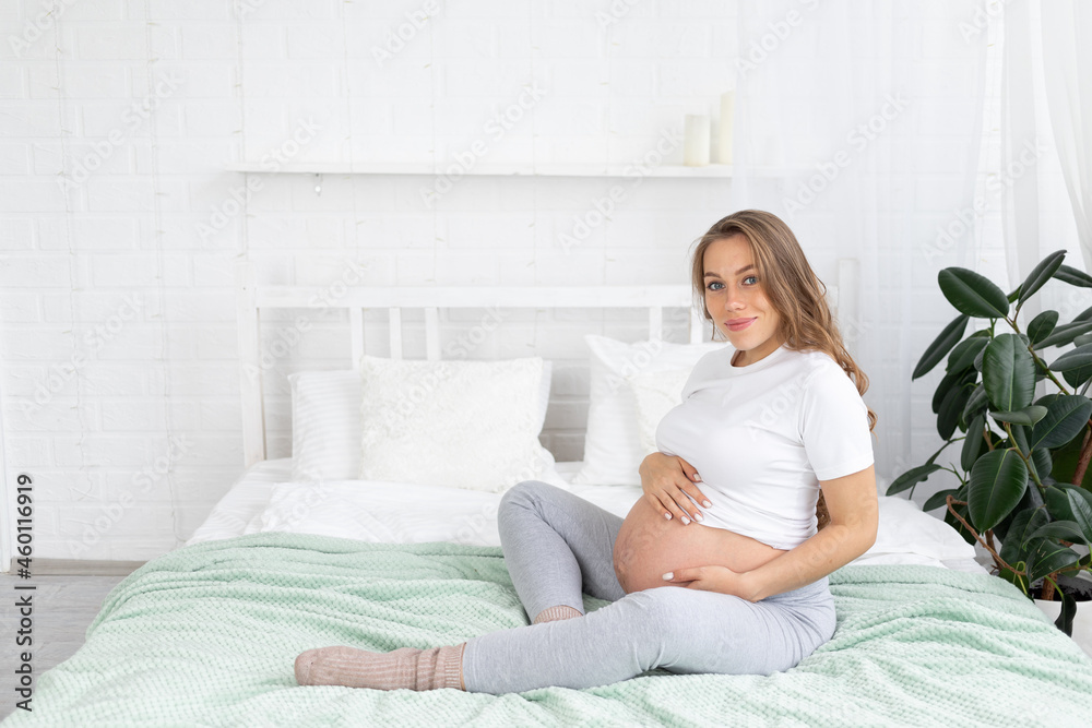 a pregnant woman is a young happy expectant mother thinking about her baby and touching her stomach on the bed at home. The concept of motherhood, pregnancy, copy space a pregnant woman is a young happy expectant mother thinking about her baby and touching her stomach on the bed at home. The concept of motherhood, pregnancy, copy space