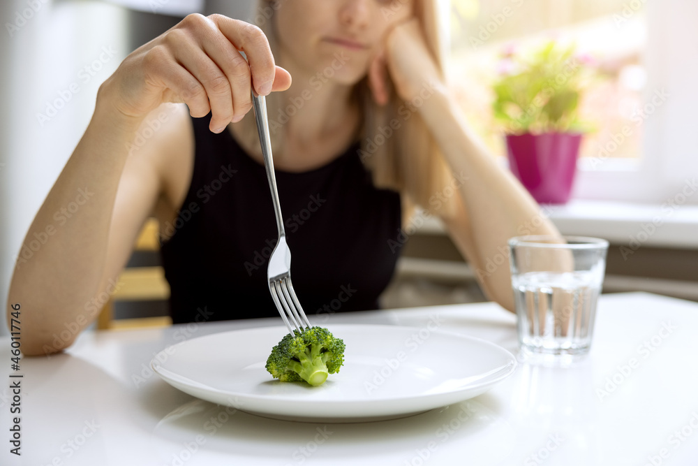 dieting problems, eating disorder - unhappy woman looking at small broccoli portion on the plate - obrazy, fototapety, plakaty 