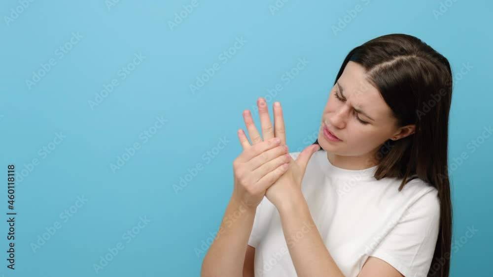 Closeup of tired young female arms holding her painful wrist caused by prolonged work, isolated on blue background. Carpal tunnel syndrome, arthritis, neurological disease concept. Numbness of hand Closeup of tired young female arms holding her painful wrist caused by prolonged work, isolated on blue background. Carpal tunnel syndrome, arthritis, neurological disease concept. Numbness of hand