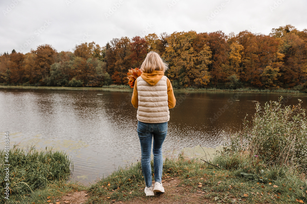 The woman is in the autumn park. Autumn atmosphere, scenic view of the river The woman is in the autumn park. Autumn atmosphere, scenic view of the river