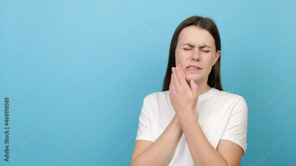 Unhappy sad young caucasian woman suffering from acute tooth pain, touching her sore jaw and frowning, isolated over blue studio background wall with copy space. Oral hygiene and toothcare concept Unhappy sad young caucasian woman suffering from acute tooth pain, touching her sore jaw and frowning, isolated over blue studio background wall with copy space. Oral hygiene and toothcare concept