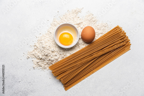 Ingredients for making whole grain pasta on light background. Integral brown spaghetti healthy alternative