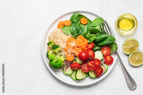 Salad with quinoa, spinach, broccoli, tomatoes, cucumbers and carrots, served on plate with white background and copy space. Clean healthy food concept