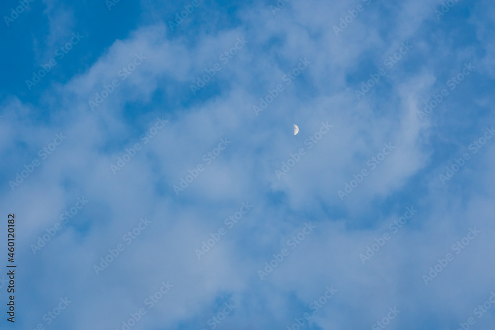 Half moon on blue bright sky background and clear clouds on daytime