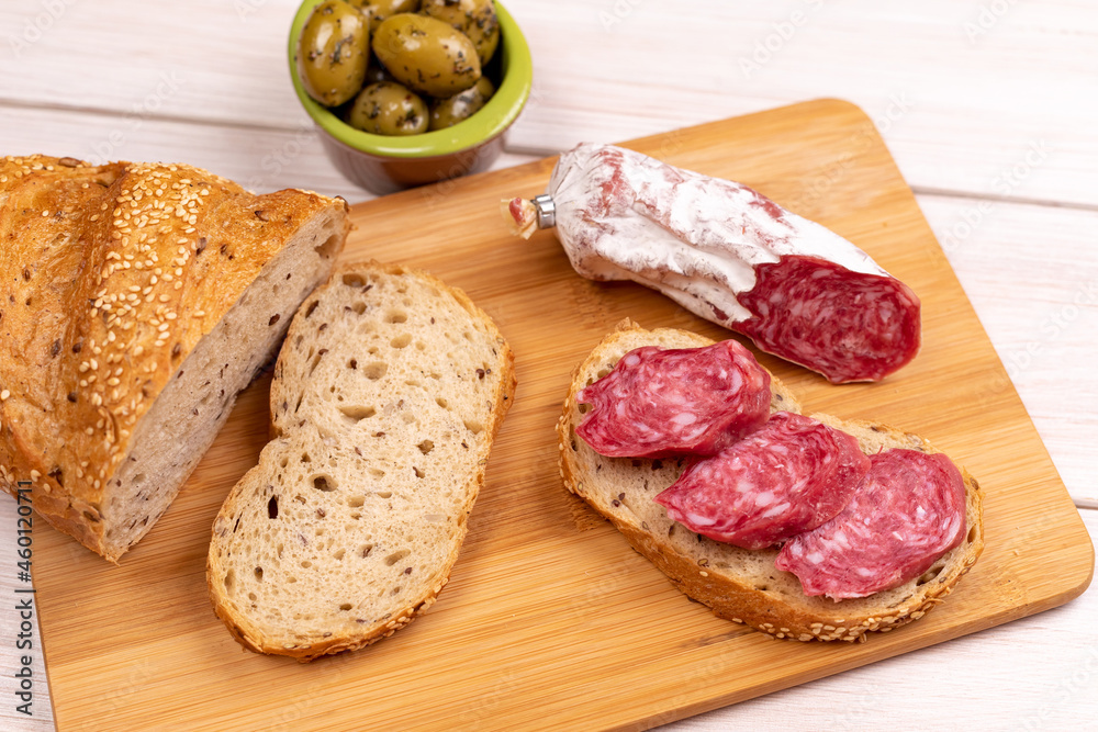 Sandwich of dried sausages, olives and loaf of whole grain bread on wooden board. Concept of simple affordable food. View from top Sandwich of dried sausages, olives and loaf of whole grain bread on wooden board. Concept of simple affordable food. View from top