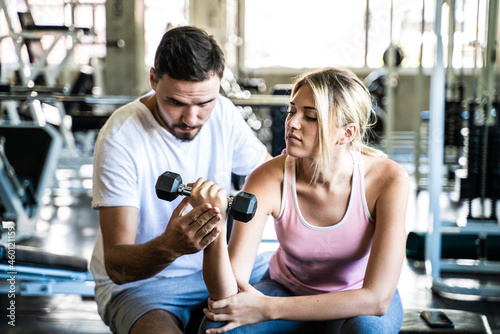 Sport women lifting dumbbell with trainer men in gym