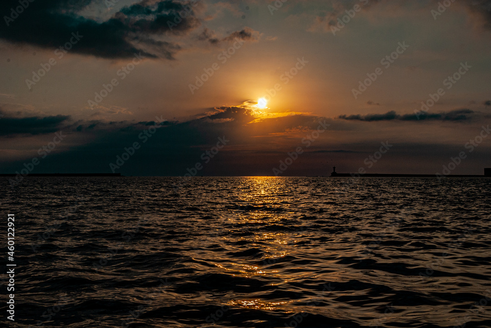 a soft calm sunset over a calm sea, when the setting sun is reflected in the water, and the sun sinks into dark clouds