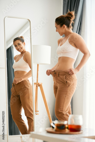 Young woman looks herself in mirror and feels satisfied after loosing weight.