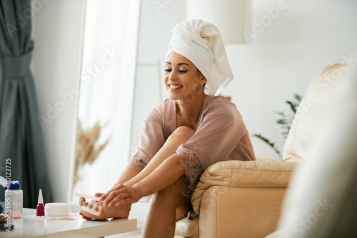 Young happy woman uses nail file while giving herself pedicure at home.