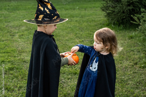 two small children in Halloween costumes play with pumpkins in the yard. Happy Halloween. photo