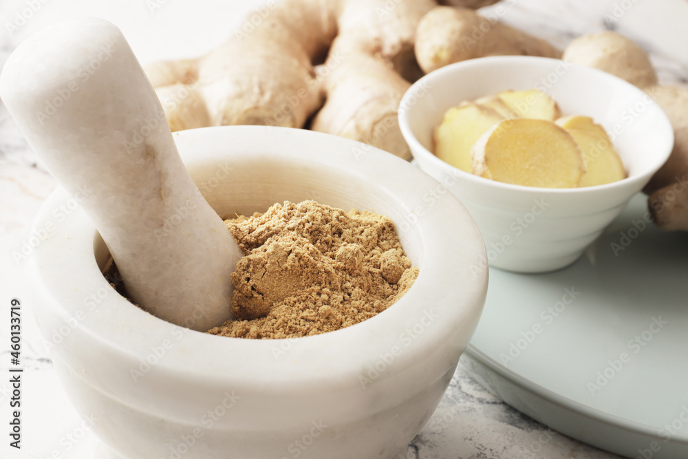 Ground ginger in a mortar, fresh ginger in the background, ginger pieces in a bowl. Spice for recipes. Health and immunity for the winter. Autumn harvesting.
