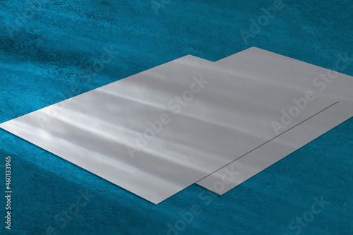 Two empty white horizontal rectangle a4 poster, business card or flyer mockups lying diagonally with overlay of rainbow light refraction caustic effect on blue concrete background. Isometric view