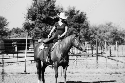 Woman mounting horse to ride horseback on western ranch in black and white.