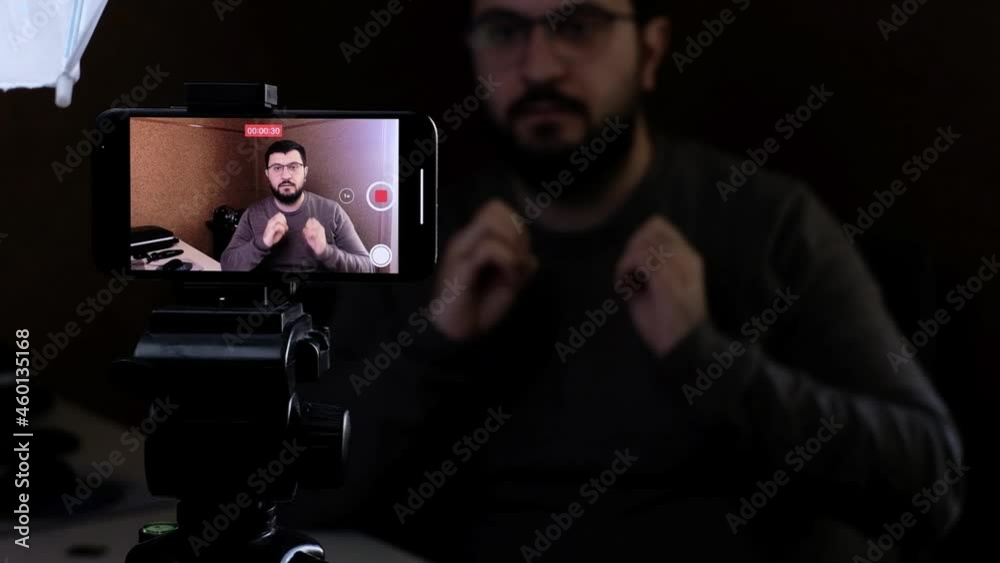 a young man, a content creator, is filming a new video in his home studio with his smartphone, because of the cheap cost of this setup and the high quality of the videos filmed on modern smartphones a young man, a content creator, is filming a new video in his home studio with his smartphone, because of the cheap cost of this setup and the high quality of the videos filmed on modern smartphones
