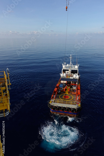 Cargo being loaded from a oil and gas platform onto a supply vessel and vessel crew give hand signal for lifting.