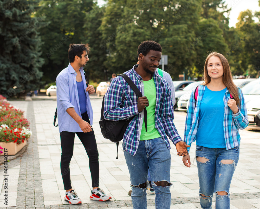 Two friends with backpacks walking and talking outdoors Two friends with backpacks walking and talking outdoors