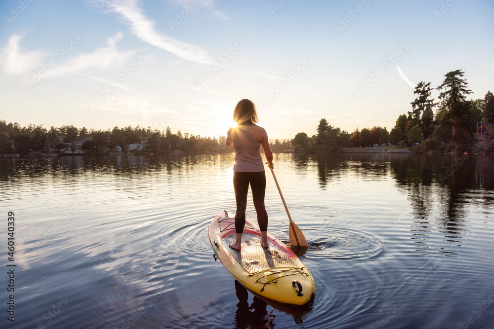 Adventurous Caucasian Adult Woman Paddling on a Stand up Paddle Board in water at a city park. Sunny Sunset Sky. Gorge Park, Victoria, Vancouver Island, BC, Canada. - obrazy, fototapety, plakaty 