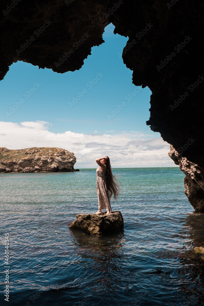 a woman on a rock looking into the distance against the sea