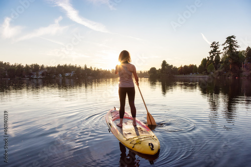Adventurous Caucasian Adult Woman Paddling on a Stand up Paddle Board in water at a city park. Sunny Sunset Sky. Gorge Park, Victoria, Vancouver Island, BC, Canada. © edb3_16