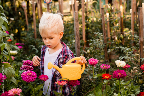 The toddler is watering flowers in the garden using a watering can